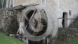 Rotating old wooden wheel of mill. Two children entering mill.