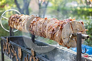 A rotating spit roast of meat over hot coals. Grill meat dish, roasted pork on spit