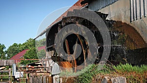 Rotating water mill. Old wooden water mill. Mill wheel rotating under stream of water at village with traditional red roofed house
