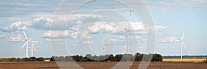 Rotating wind generators in the field against the cloudy sky on sunny summer day.