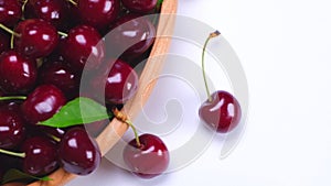 Rotating wooden bowl with ripe red cherries on a white background