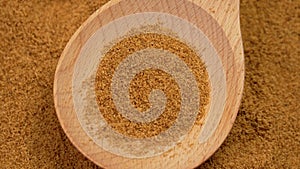 Rotation of brown organic coconut sugar granules in a wooden spoon