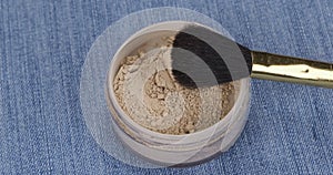 Rotation of cosmetic lying on denim. Powder and brush.