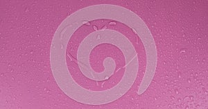 Rotation of water drops in the shape of a heart on a pink background