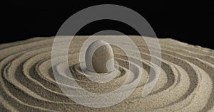 Rotation of a white stone in the center of a sandy concentric spiral. Close-up of patterns in the sand. Sand texture