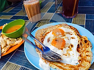 Roti sarang burung, a pratha looks like bird nest with half cook eggs in the middle served with teh tarik as staple breakfast in