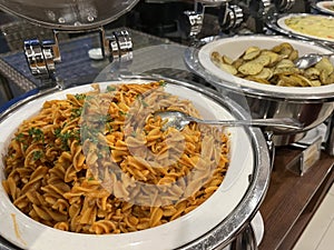 Rotini or spiral pasta with tomato sauce in chafing dish.