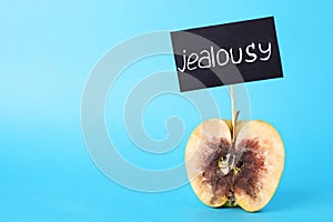 Rotten apple with JEALOUSY sign on blue background. Space for text