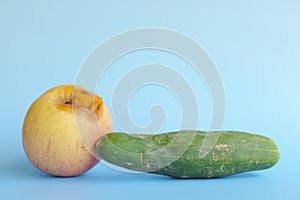 Rotten, bruised, stale or bad apple and cucumber isolated in blue background. Food waste and poor agricultural crop quality concep