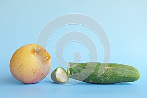 Rotten, bruised, stale or bad apple and cucumber isolated in blue background. Food waste and poor agricultural crop quality concep