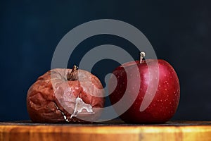 A Rotten and a Fresh Red Apple Next to Each Other. Good vs Bad. Antithesis Concept. Side View. Dark Background