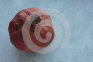 Rotten pomegranate on a table. Spoiled fruit on gray concrete background.