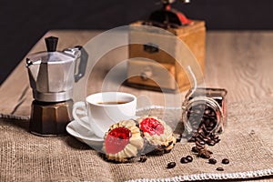 On a rough burlap is coffee maker mocha, vintage grinder, glass jar with roasted coffee beans. On the white saucer there