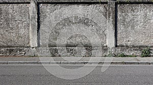 A rough concrete wall with a gray sidewalk and an asphalt road. Urban background for copy space