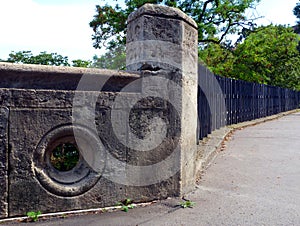 Rough gray stone railing olong public street and black steel fence beyond