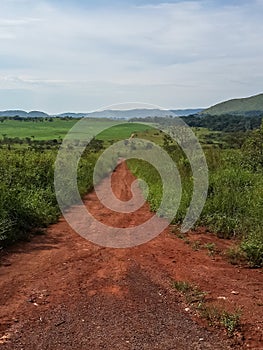 Rough and narrow red dirt road leading through green and mountainous landscape of rural Angola, Africa