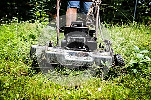 Rough old cottage lawnmower pushes through thick grass and weeds.