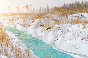 Rough river at the foot of the mountains in a turquoise, blue, green forest in winter, ice and snow around the landscape.