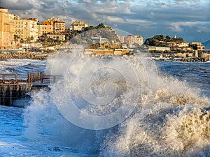 Rough sea waves crashing over a pier in the city of Genoa Genova, mediterranean sea, ligurian coast, Italy.