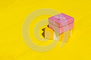 Rough shadow. Bright sunshine. Retro yellow wooden background. Gift box in pink
