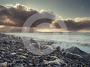 Rough stone beach at dusk, dark dramatic sky with sun light beams,