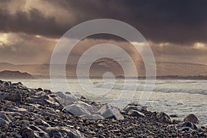 Rough stone beach at dusk, dark dramatic sky with sun light beams, Strandhill town, county Sligo, Ireland, Atlantic ocean. Nobody