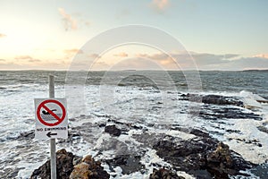 Rough stone coast line Atlantic ocean, West coast of Ireland, Sligo. No swimming sign, Pastel sunset sky