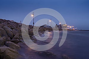 Rough stone coast of Salthill, Galway city Ireland. Blue hour. Town illumination reflects in calm water of the ocean. Calm and