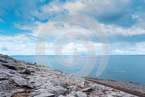 Rough stone terrain, small road and blue water and sky over Galway bay, Ireland. Nobody, Irish nature landscape. Warm sunny day.