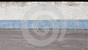 Rough stucco wall painted in light blue and white with a sidewalk and an asphalt  street in front. photo