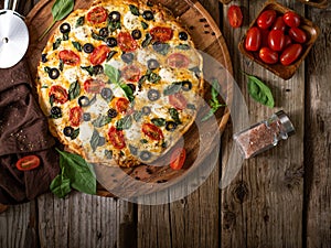 On a rough wooden table in a rustic style, we see pizza on a wooden plate, also on the table are green mint leaves, tomatoes,