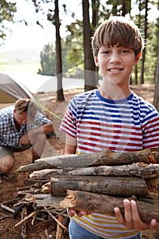 Roughing it with dad. a young boy gathering firewood during a camping trip with his father.