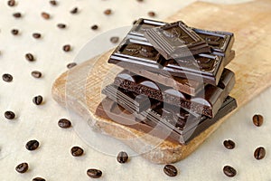 Roughly broken pieces of chocolate are stacked on a wooden board, coffee beans are scattered around