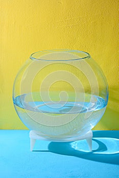 Round aquarium with water stands on a yellow table. Blue background.