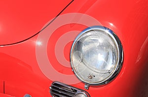 Round automotive headlamp of expensive vintage luxury red car close-up