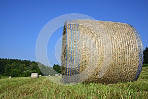 A round bale of hay on a freshly mown meadow against a blue sky