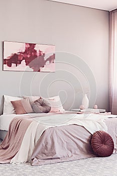 Round beige pillow on white bed in classy bedroom interior with abstract painting on the wall