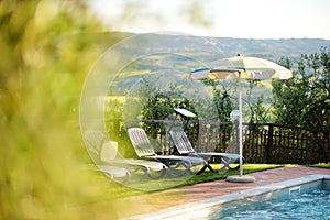 Round beige sunshade and several folding beach chairs by the outdoor pool in agriturismo overlooking fields and farmlands of