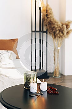 Round black table with burning candles and incense stick in bedroom interior