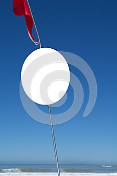 Round blank sign in blue sky with red flag on beach