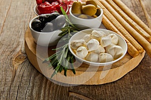 Round board with rosemary, breadsticks and bowls with antipasto ingredients