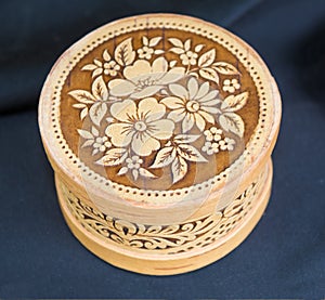 A round box of birch bark decorated with an elegant floral pattern on a dark blue background