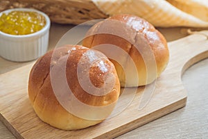 Round bun, bread rolls on wooden plate and pineapple jam