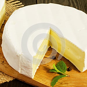 Round Camembert cheese, sliced, with a mint branch and pepper pe