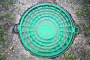 Round cast-iron turquoise hatch with a pattern of divergent rings of turquoise rays on the background of green grass