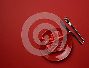 Round ceramic plate and fork with knife on red background, festive table setting