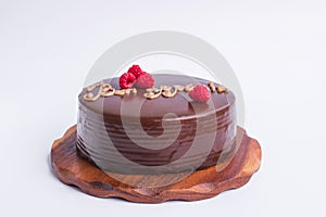 A round chocolate cake with raspberry decor and the inscription - Bon appetit. On a wooden stand isolated on a white background.