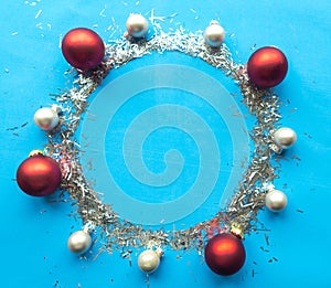 Round Christmas silver tinsel frame with baubles and snowflakes on bright blue background.