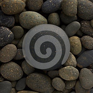 Round circle shape of big sea stone laid on a pile of nature pebbles or a group of rocks.