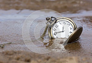 Round clock with hands lying on the wet sand, water, time